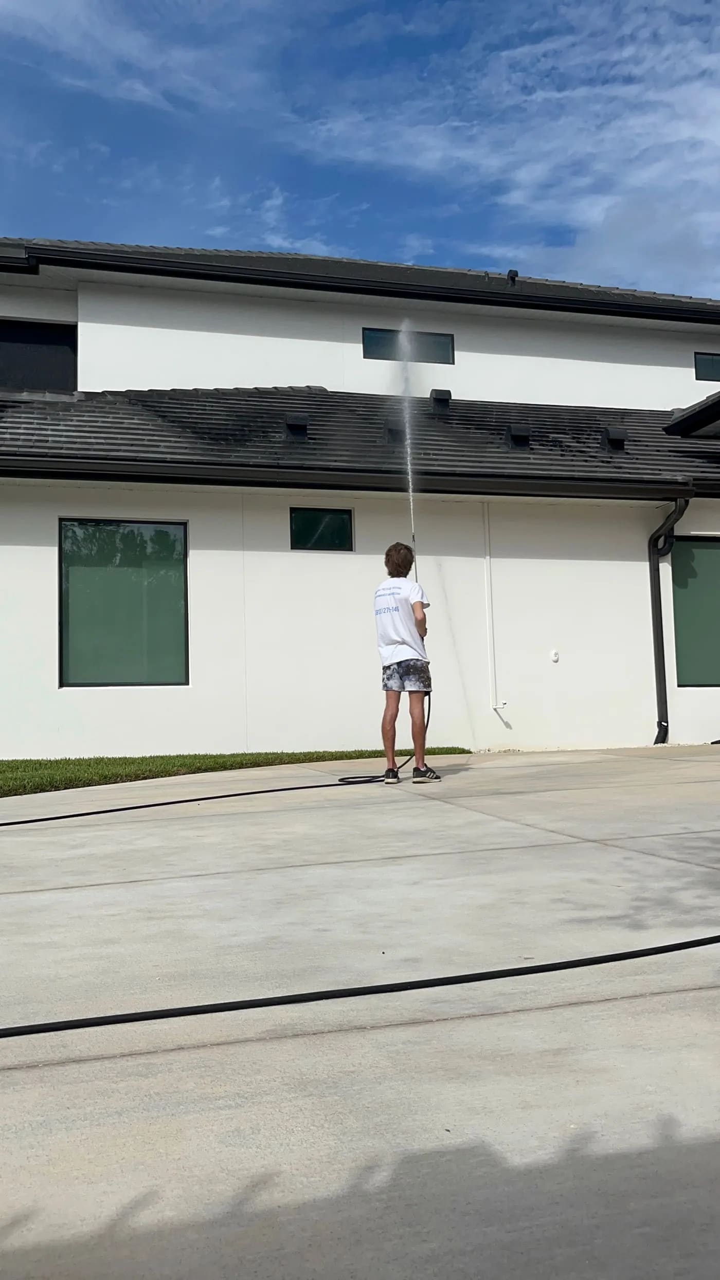 Technician cleaning a large Tampa-area house exterior and roofline